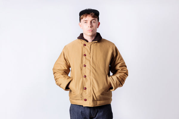 Person wearing a tan jacket with red buttons on a white background