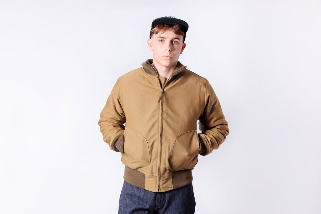 Person wearing a brown bomber jacket and cap on a white background