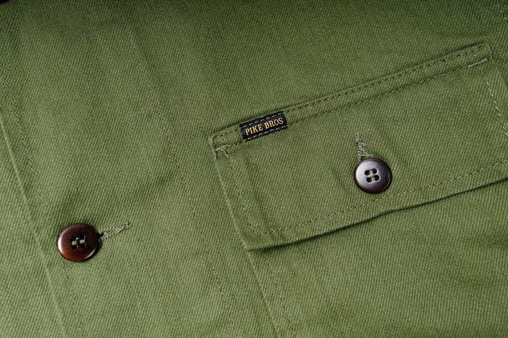 Close-up of a green fabric pocket with buttons and a brand label.