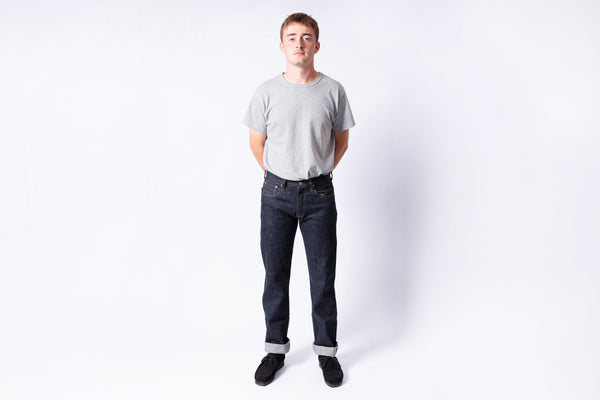 Person wearing a gray t-shirt and dark jeans on a white background