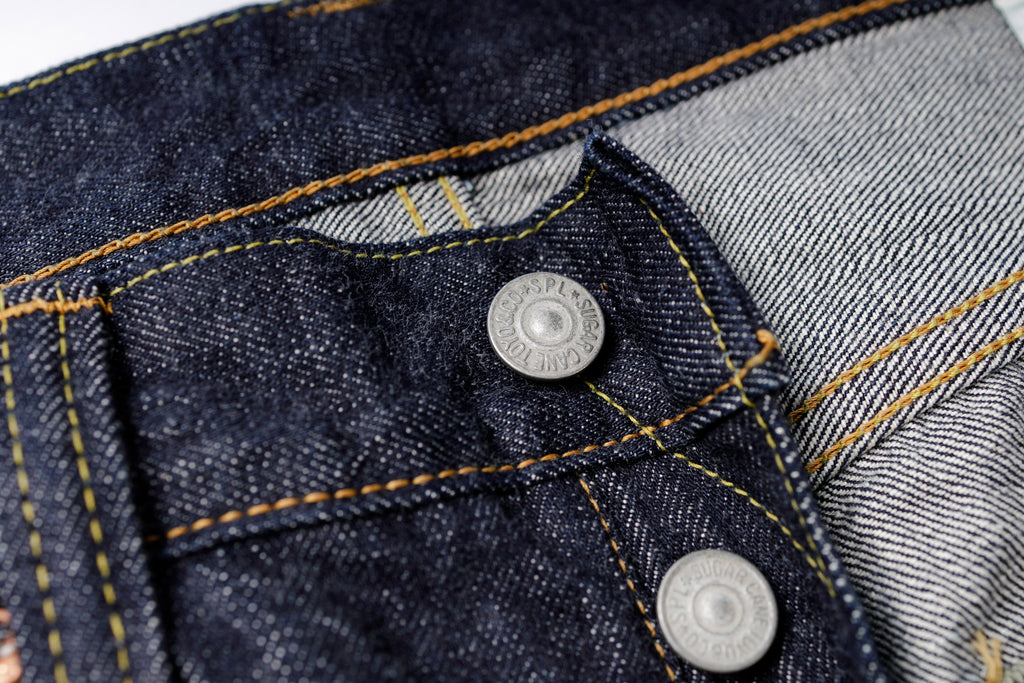 Close-up of a button on a pair of blue jeans with stitching details.