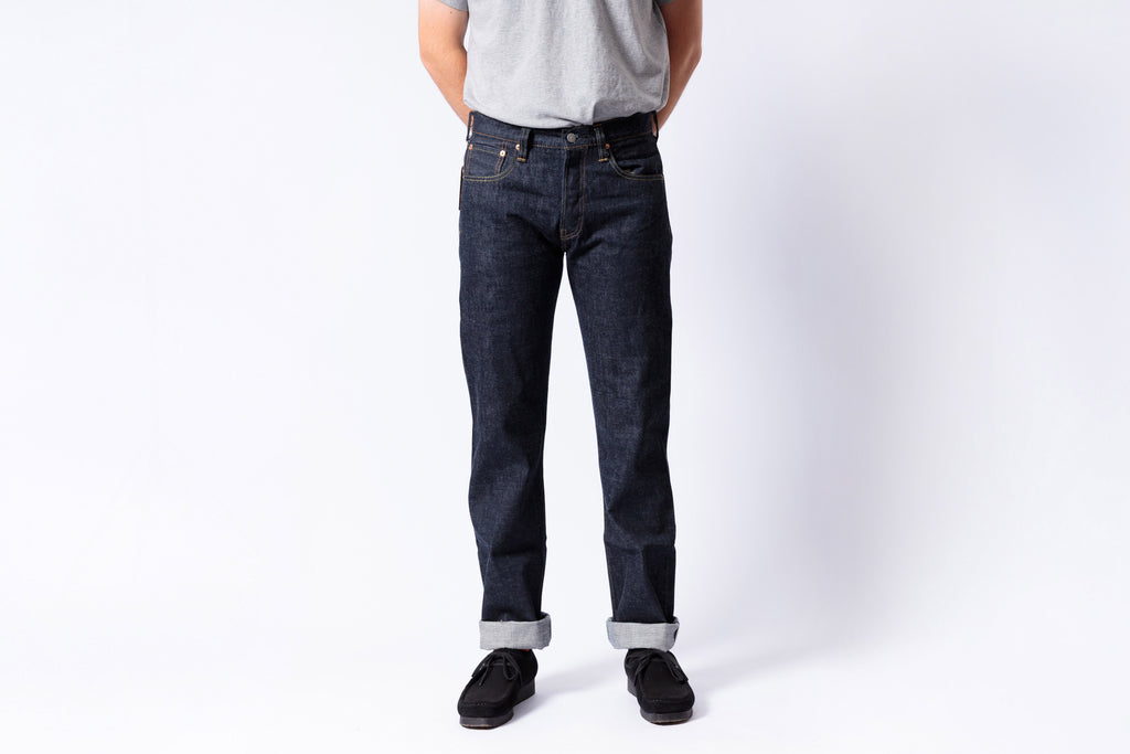 Person wearing dark blue jeans and a gray shirt on a white background