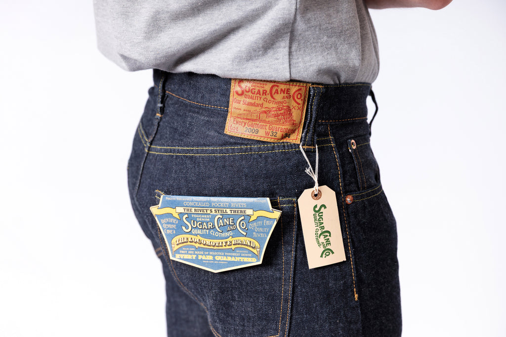 Person wearing dark blue jeans with visible brand labels on a white background