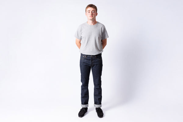 Man wearing a gray t-shirt and dark jeans standing against a white background