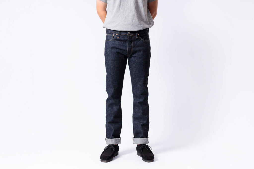 Person wearing dark blue jeans and black shoes on a white background