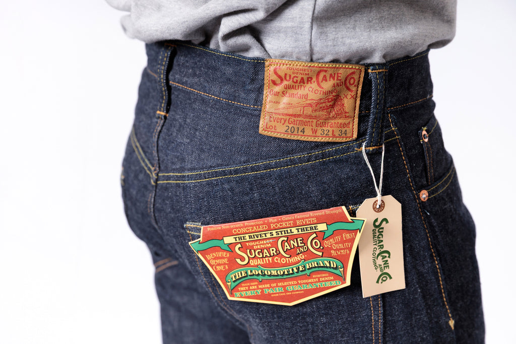 Close-up of a person wearing blue jeans with visible brand labels on a white background