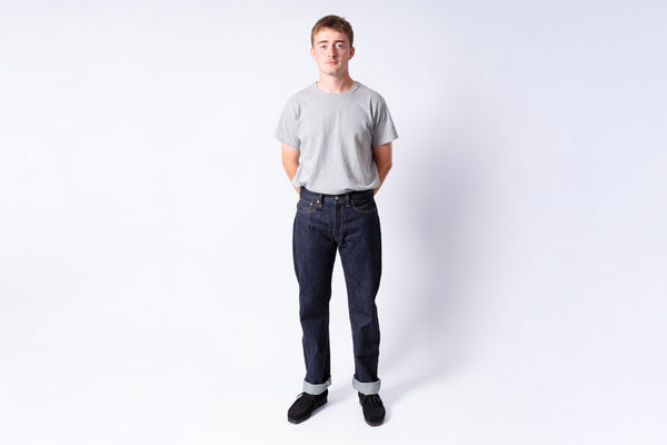 Man wearing a plain gray t-shirt and dark jeans on a white background