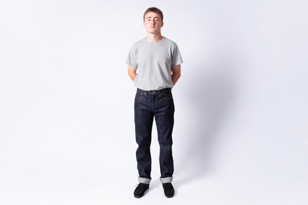 Man wearing a gray t-shirt and dark jeans standing against a white background