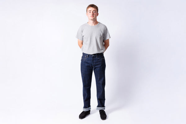 Man wearing a gray t-shirt and blue jeans standing against a white background