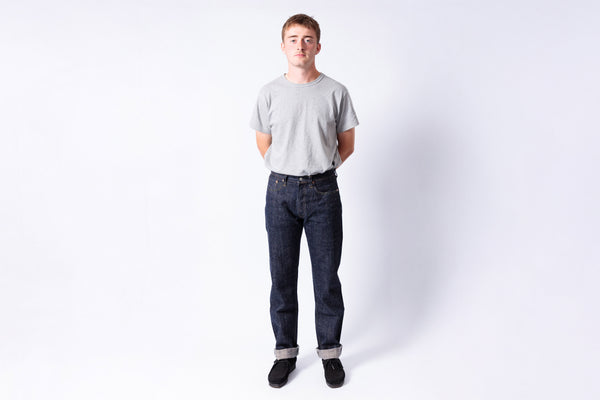 Person wearing a gray t-shirt and dark jeans on a white background