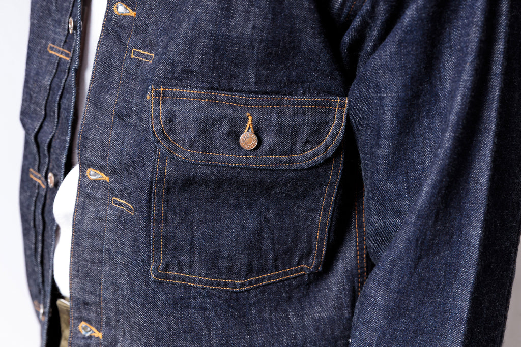 Close-up of a blue denim jacket with a pocket detail on a white background