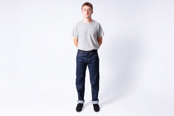 Person wearing a plain gray t-shirt and dark blue jeans on a white background