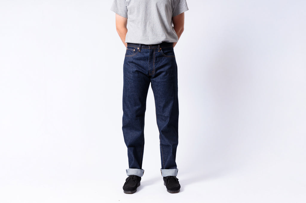 Person wearing dark blue jeans and a light gray shirt on a white background