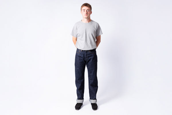 Man wearing a gray t-shirt and dark jeans on a white background