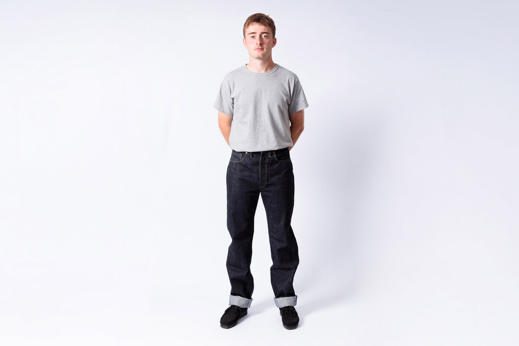 Person wearing a gray t-shirt and dark jeans on a white background