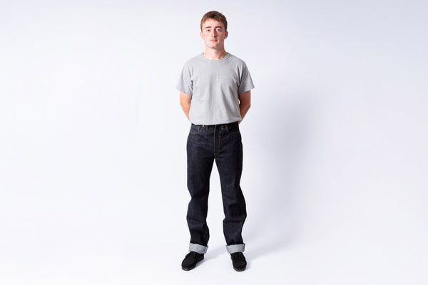 Person wearing a gray t-shirt and dark jeans on a white background