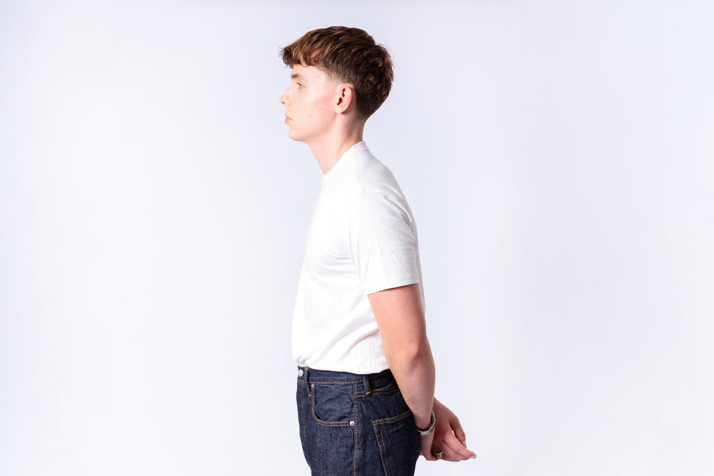 Person wearing a white t-shirt and dark jeans on a plain background