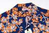 A close-up of a vintage Hawaiian shirt featuring a bold orange and white hibiscus flower and leaf pattern on a navy blue background. 