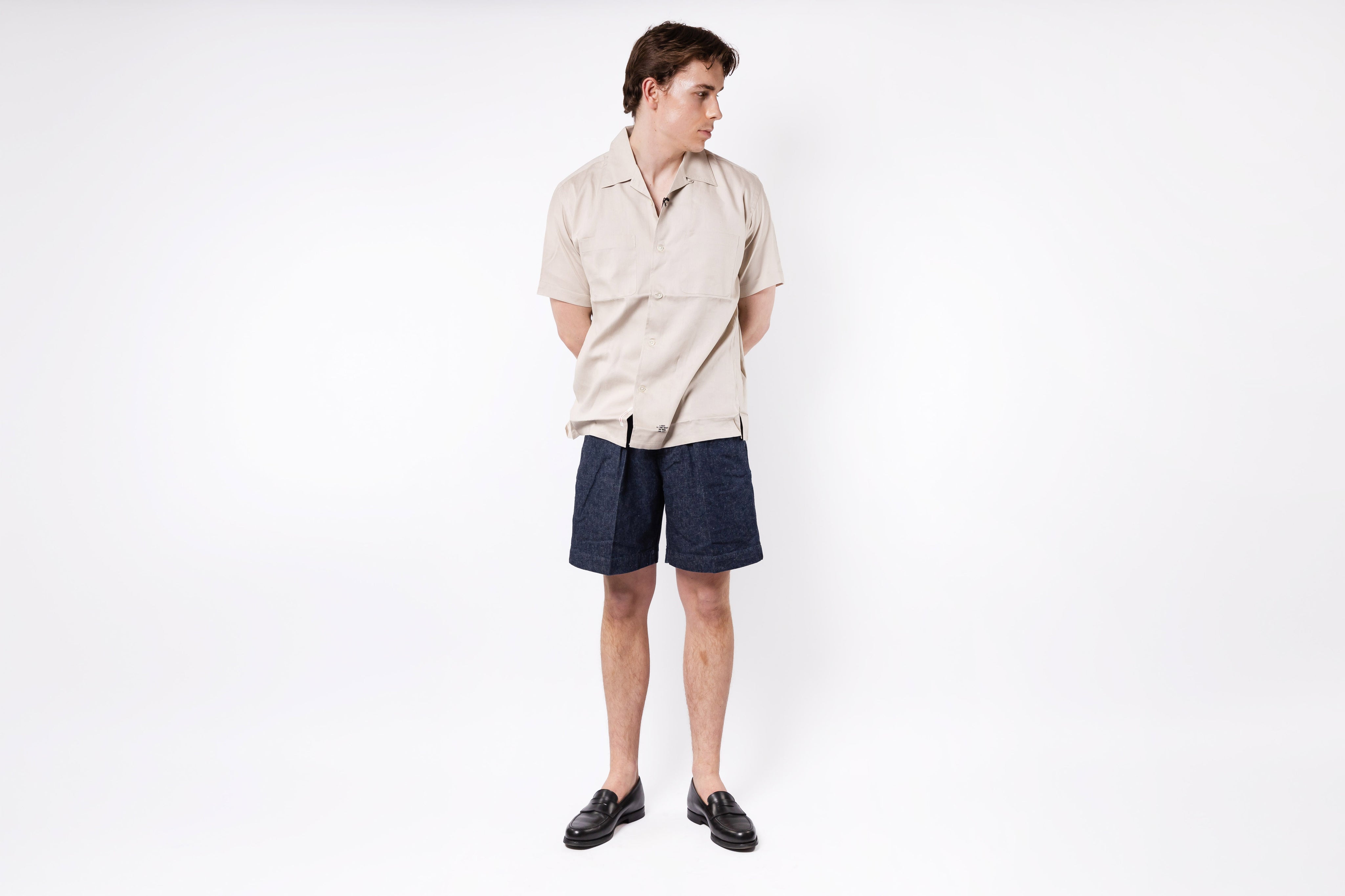 Person wearing a beige shirt and dark shorts on a white background