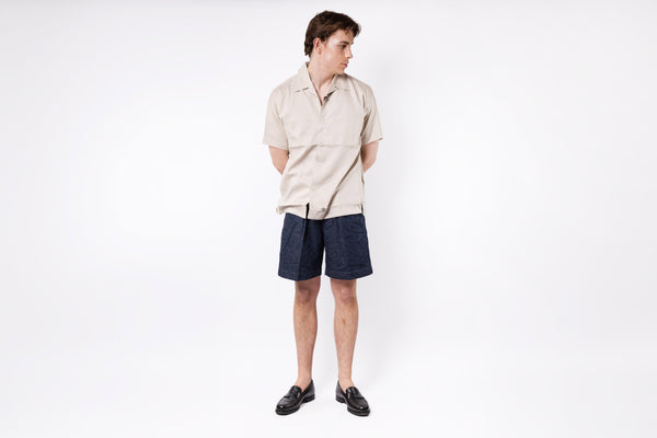 Person wearing a beige shirt and dark shorts on a white background