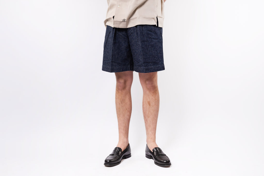 Person wearing navy shorts and a beige top on a white background