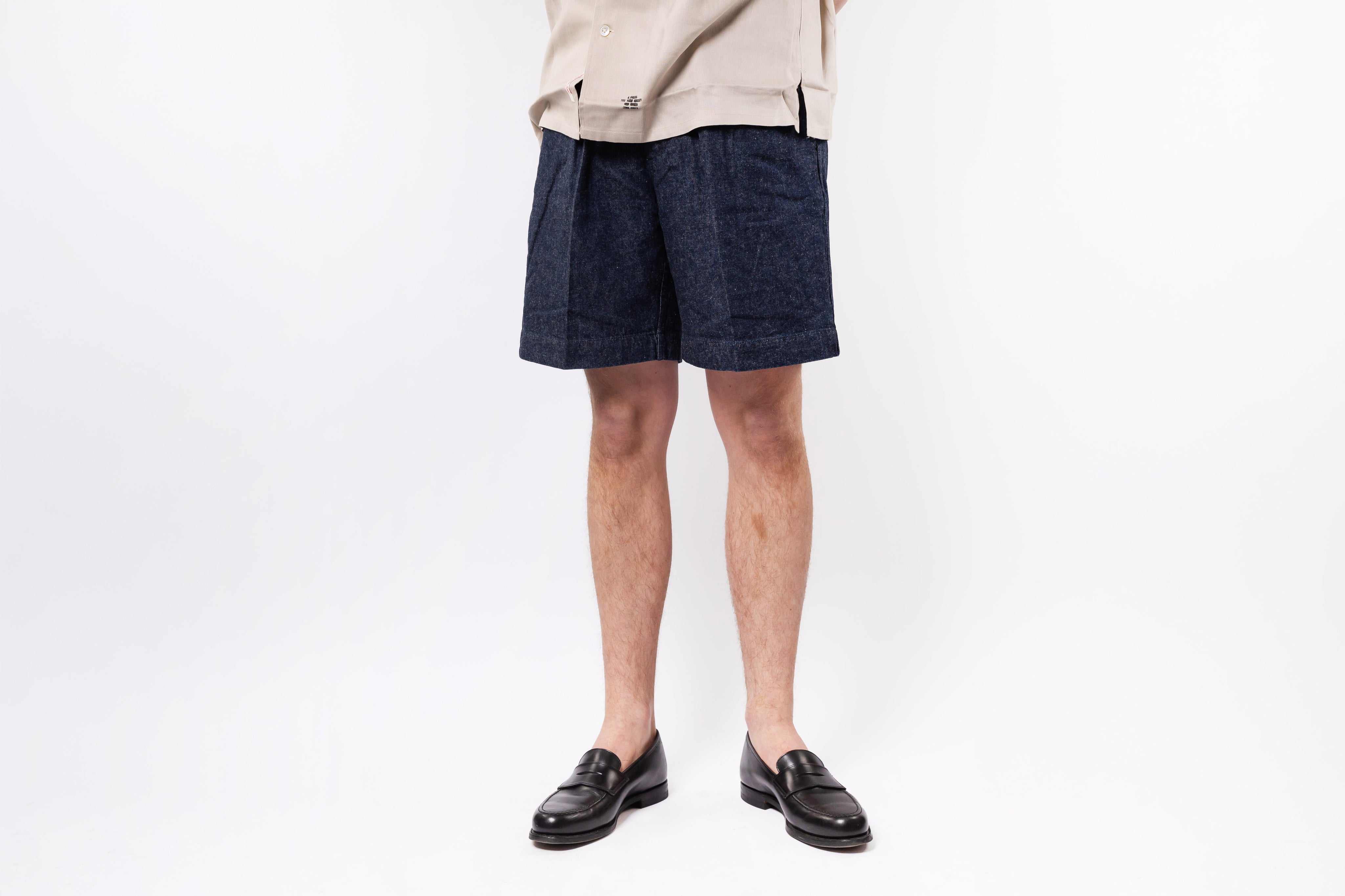 Person wearing navy shorts and a beige top on a white background
