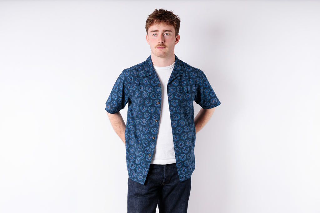 Man wearing a blue patterned shirt over a white t-shirt on a white background
