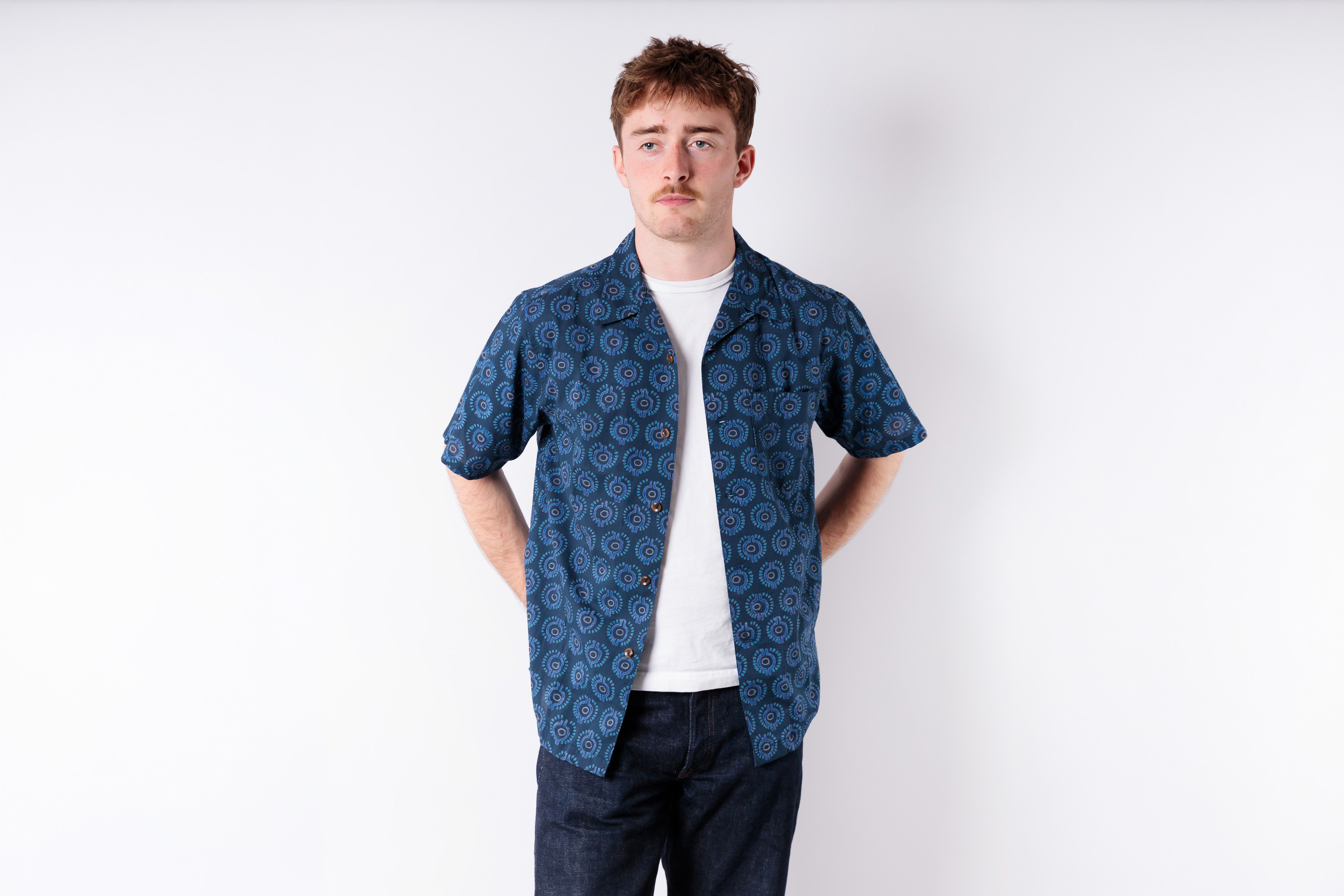 Man wearing a blue patterned shirt over a white t-shirt on a white background
