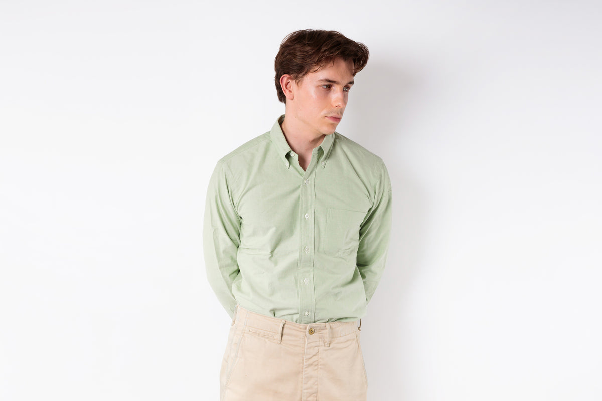 Man wearing a light green shirt and beige pants against a white background