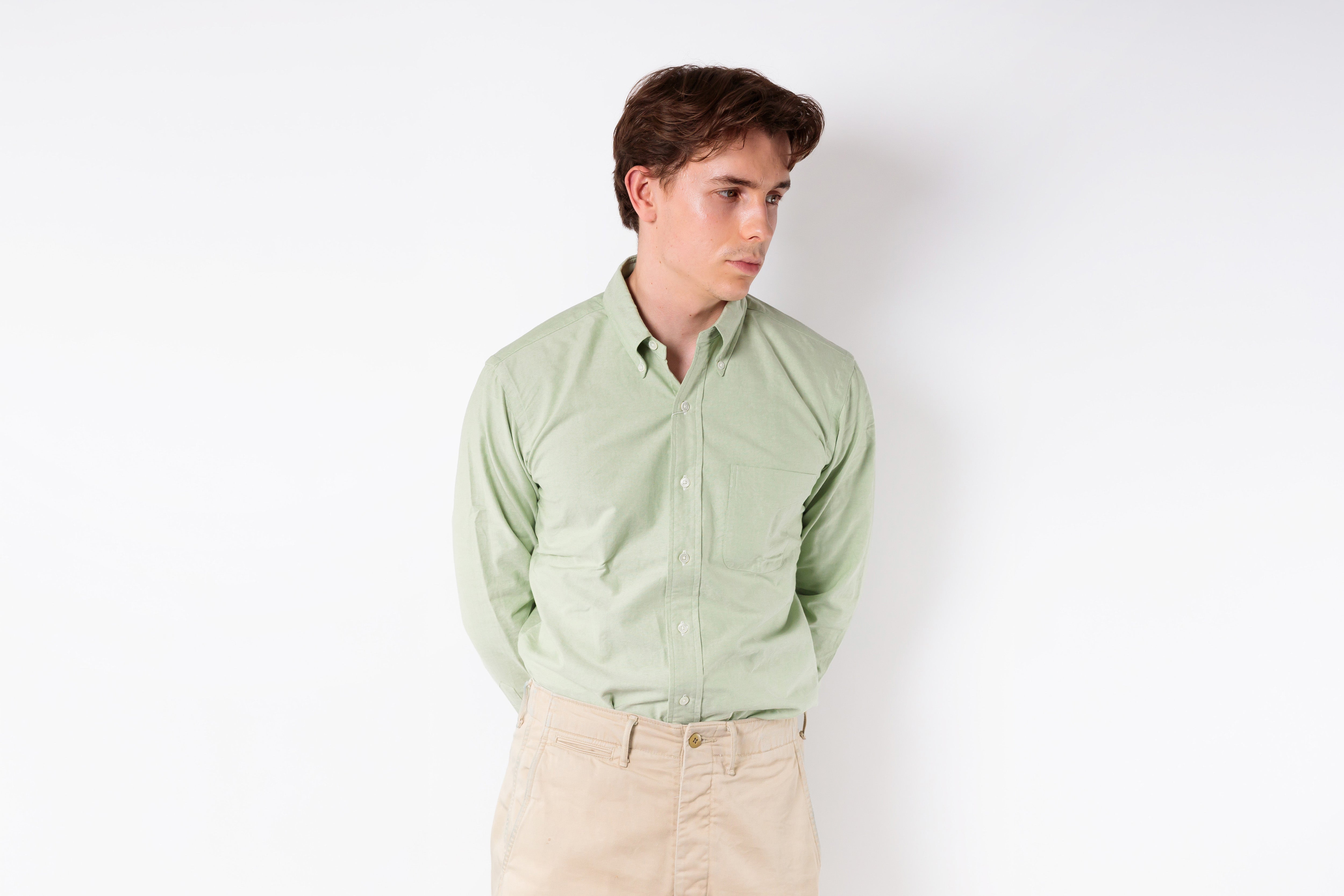 Man wearing a light green shirt and beige pants against a white background