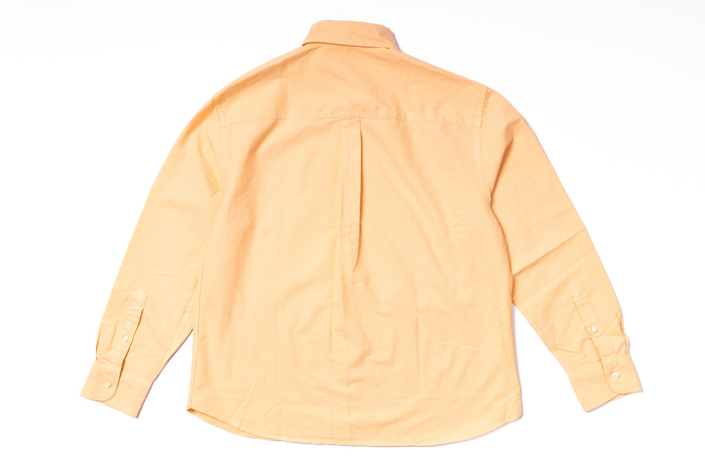 Back view of a light orange shirt on a white background