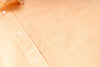Close-up of a light peach-colored shirt with buttons and a pocket.