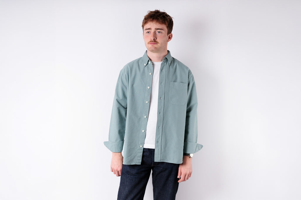 Man wearing a light green shirt over a white t-shirt on a white background