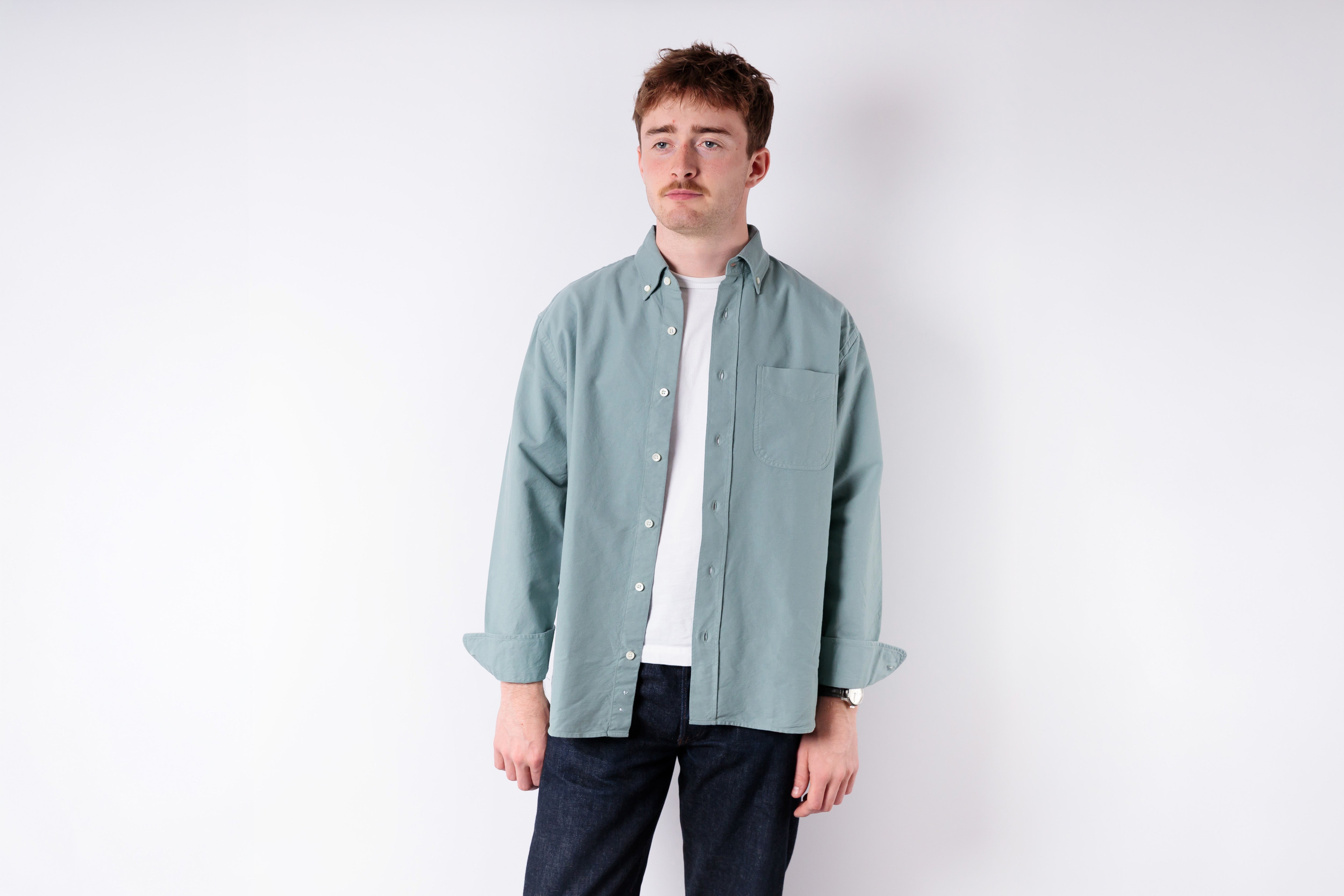 Man wearing a light green shirt over a white t-shirt on a white background