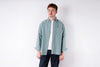 Man wearing a light green shirt over a white t-shirt on a white background