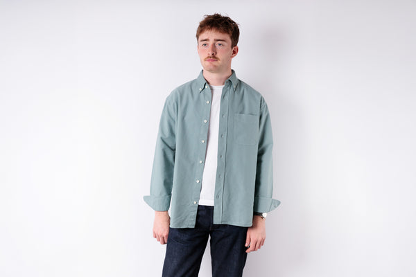 Man wearing a light green shirt over a white t-shirt on a white background