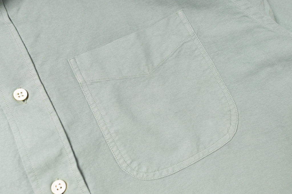 Close-up of a light gray shirt with a pocket and button details.