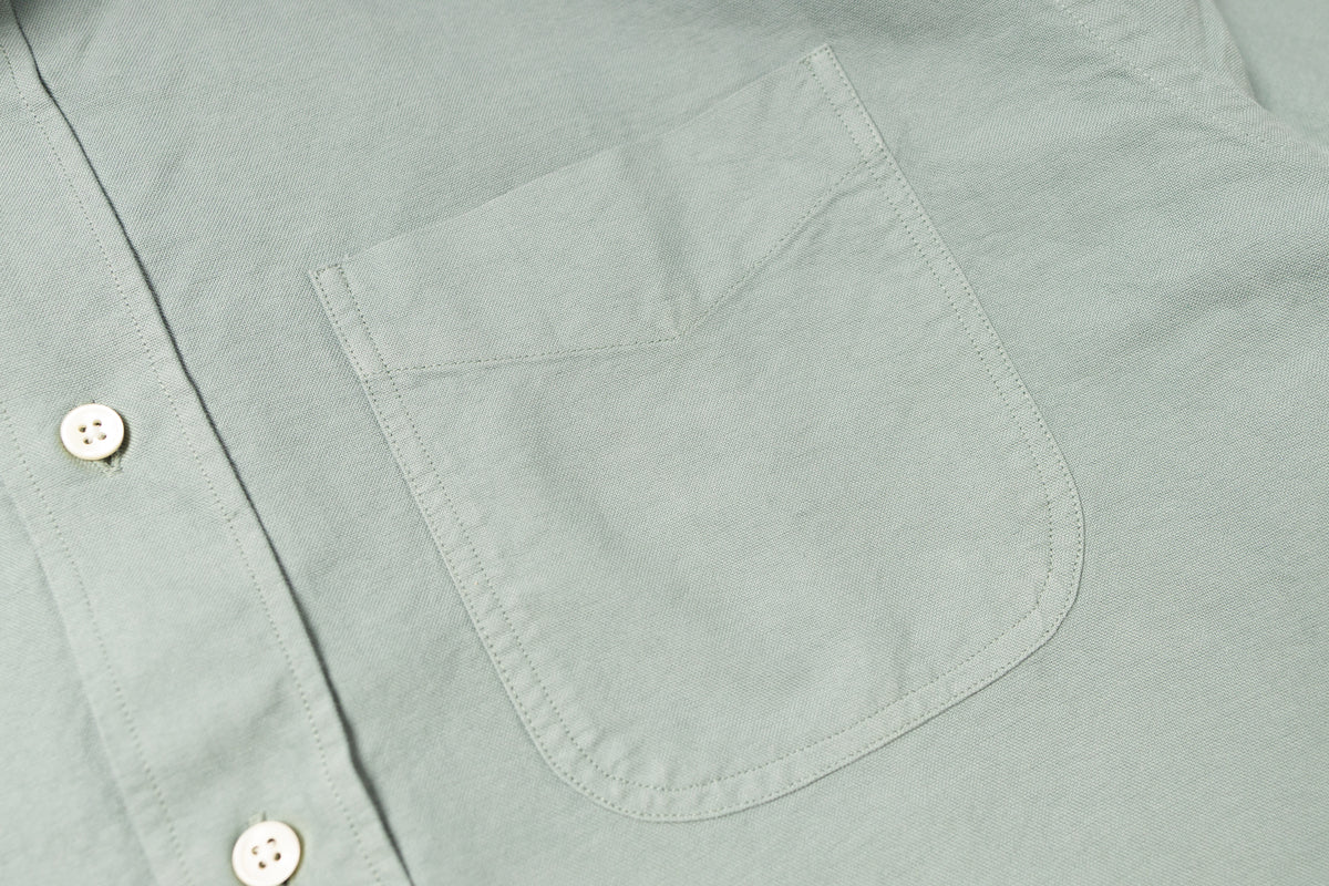 Close-up of a light gray shirt with a pocket and button details.