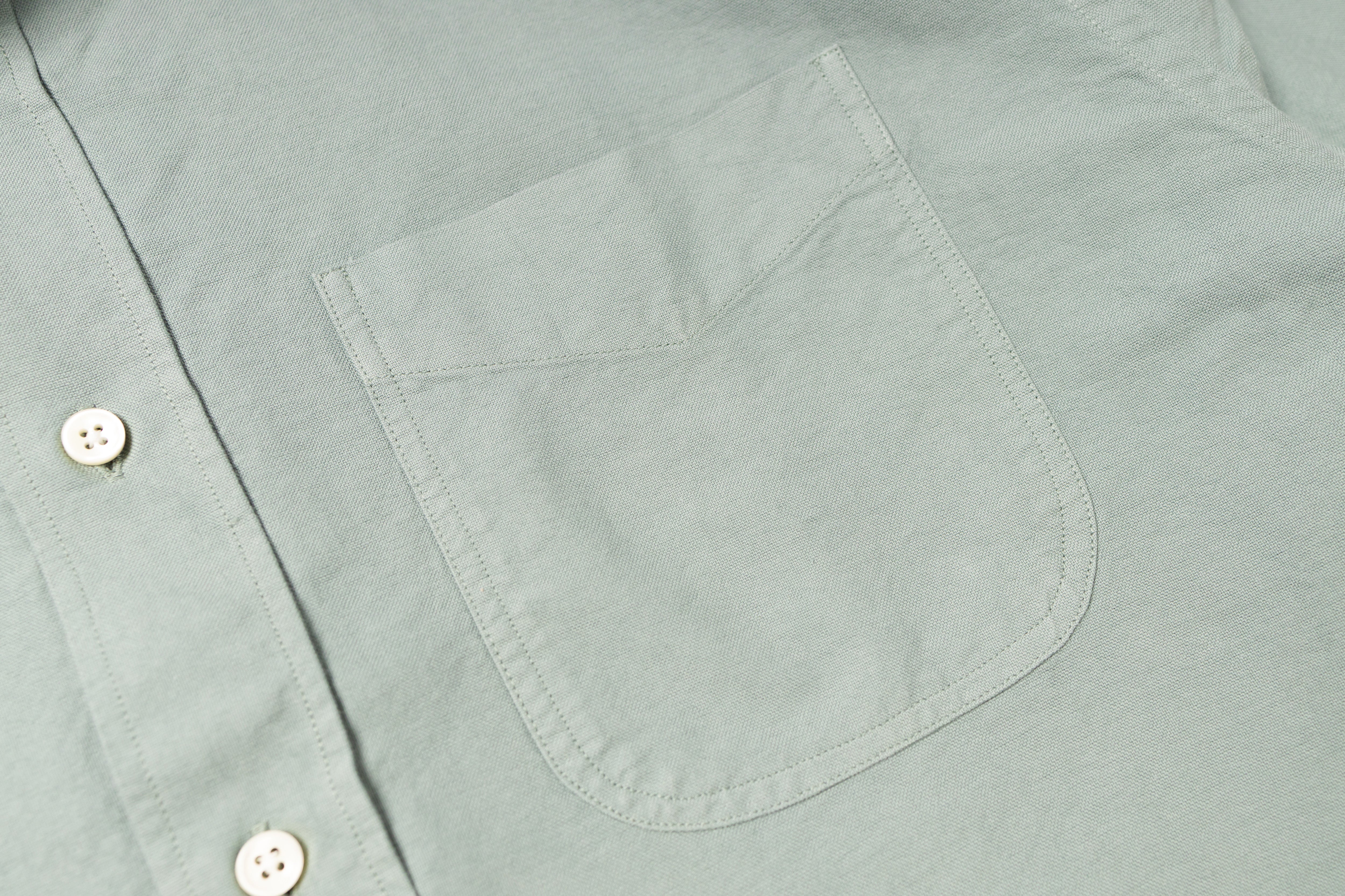 Close-up of a light gray shirt with a pocket and button details.