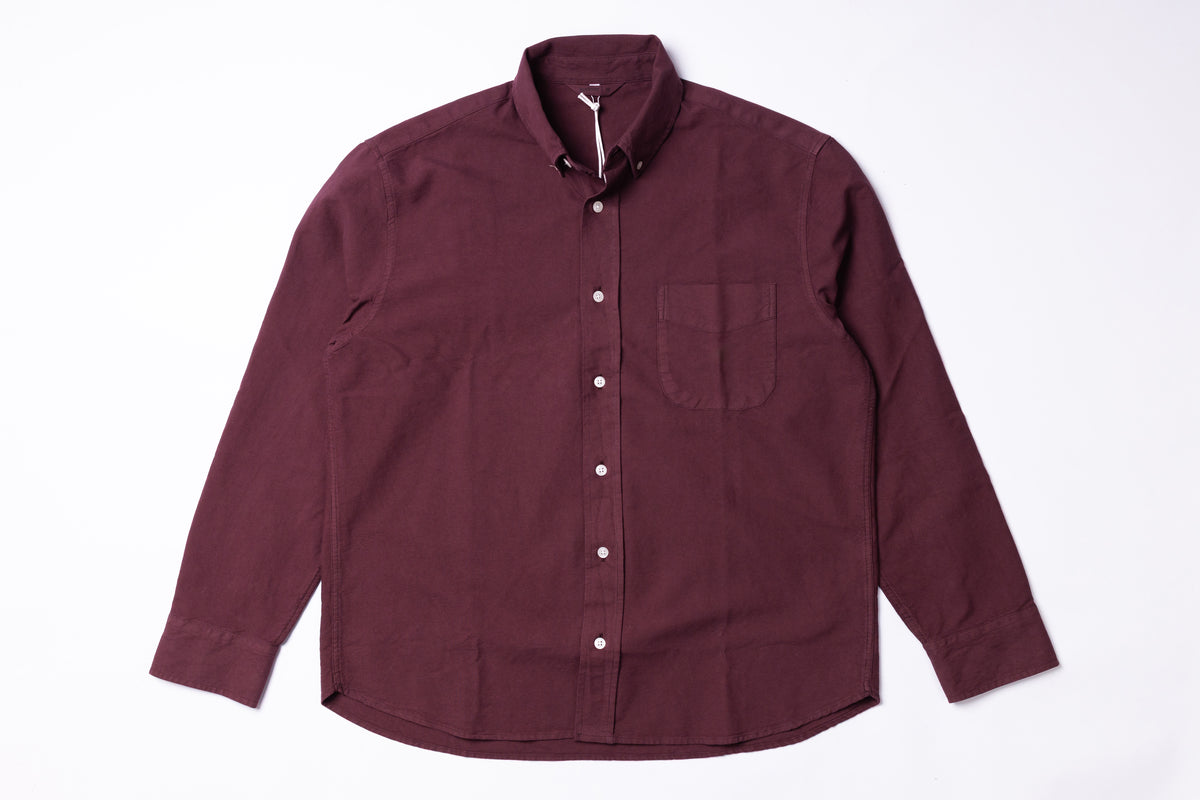 A long-sleeve button-up shirt in a deep burgundy color, laid flat against a clean white background. The shirt features a classic pointed collar, a vertical button placket with white buttons, and a single chest pocket on the wearer's left side.