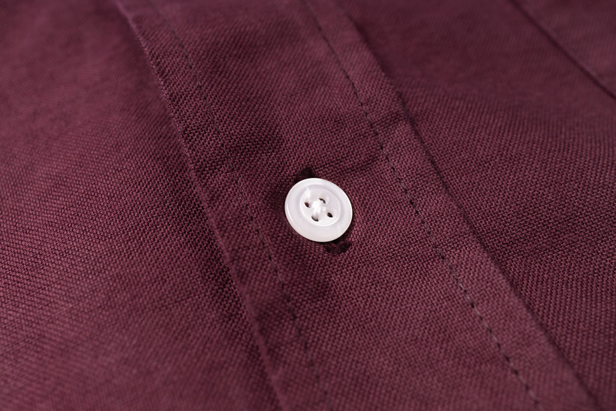Close-up of a burgundy or deep plum-colored fabric garment with a small white button near the collar placket.