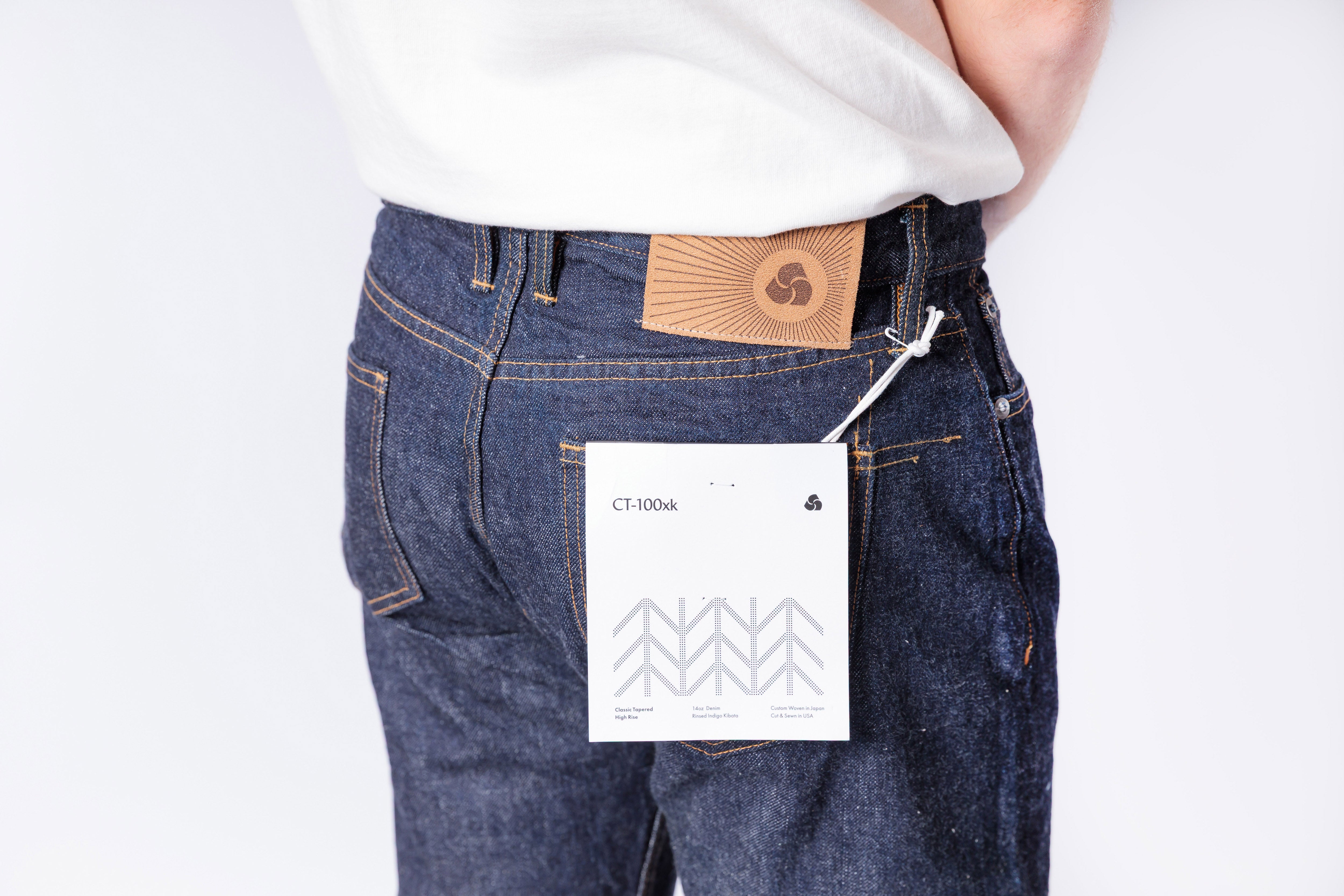 Person wearing blue jeans with a visible brand label on a plain background