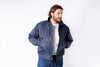 Man wearing a blue bomber jacket over a white shirt on a white background
