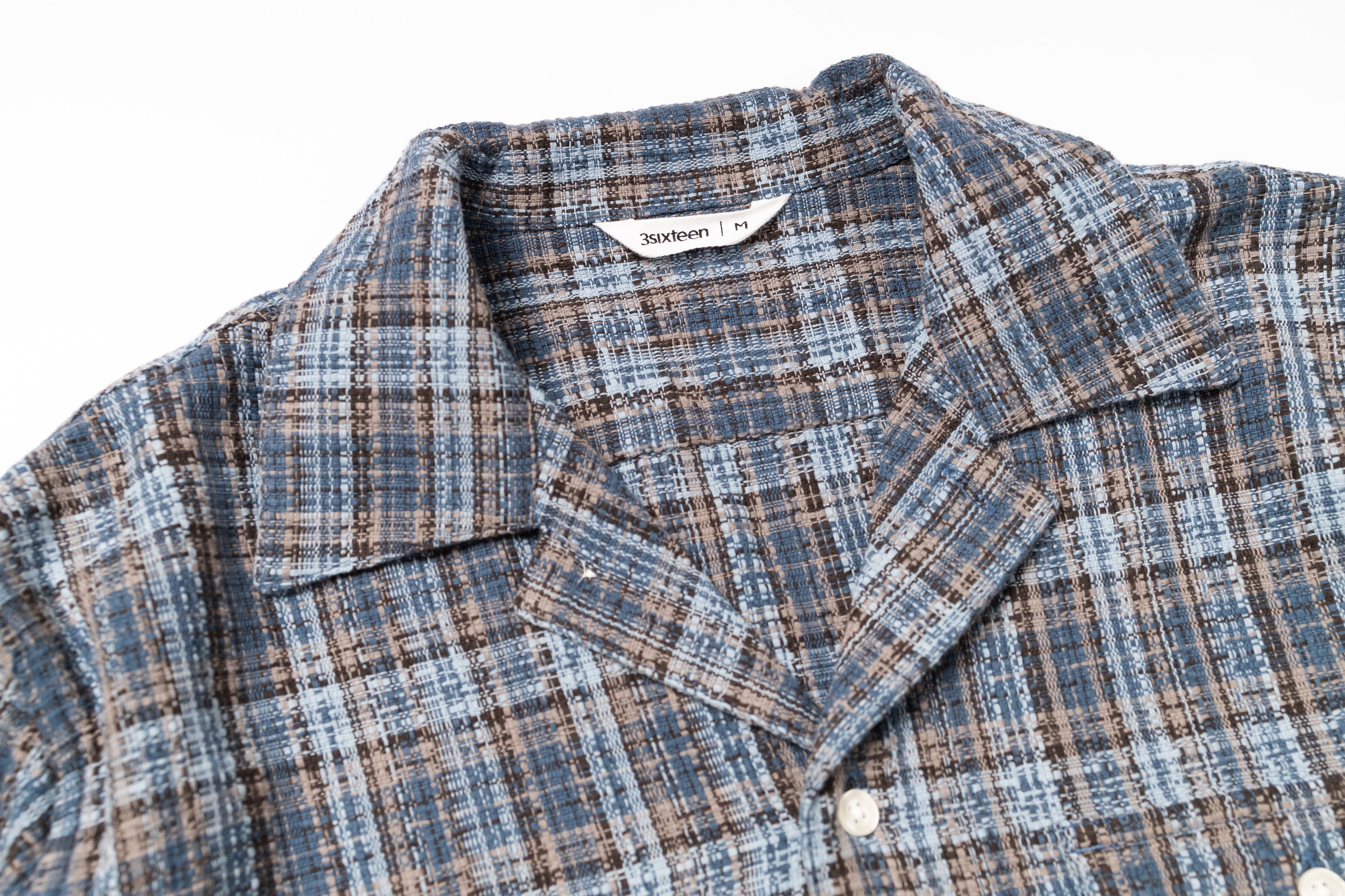 Close-up of a plaid shirt with a visible brand label on a white background