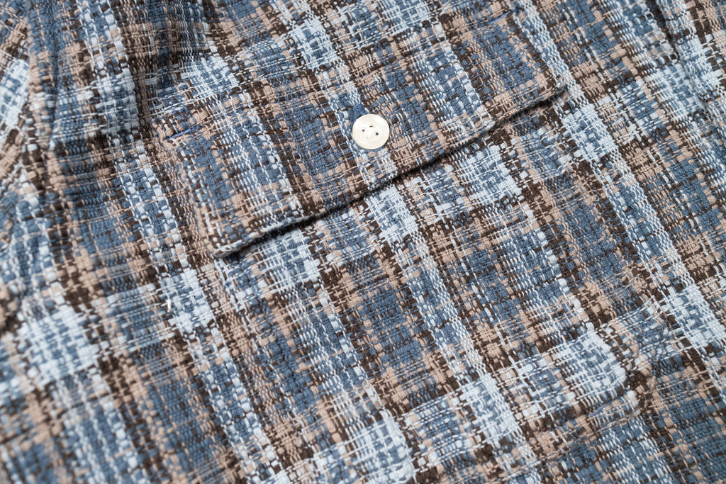 Close-up of a textured fabric with a button, featuring blue and brown plaid pattern.