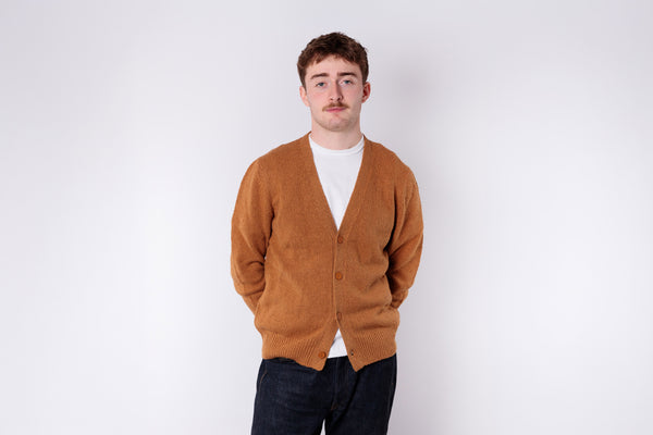 Man wearing a brown cardigan over a white shirt on a white background
