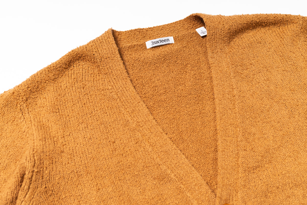 Close-up of a mustard yellow cardigan with a brand label on a white background