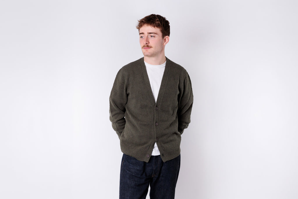 Man wearing a green cardigan over a white shirt on a white background