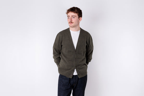 Man wearing a green cardigan over a white shirt on a white background