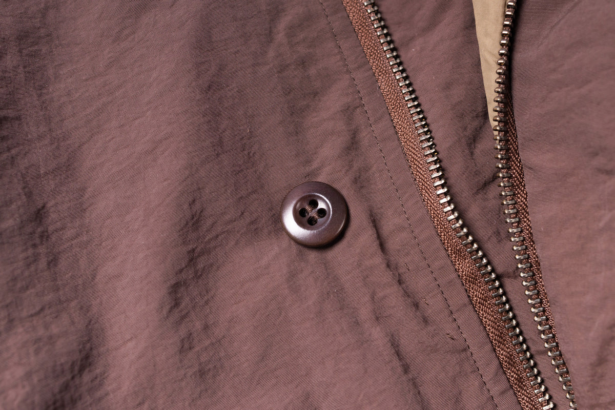 Close-up of a button and zipper on a brown fabric surface